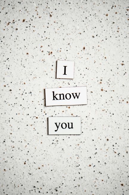 A close-up photograph of a speckled off-white terrazzo surface with small, multicoloured stone fragments embedded throughout. In the center, three white rectangular tiles with black lowercase text are